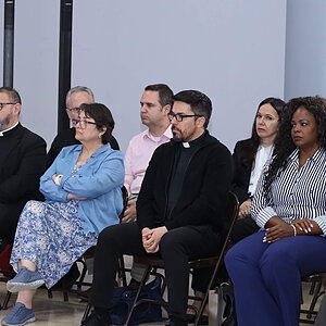 El clero y los laicos se sientan atentamente, mirando hacia adelante.